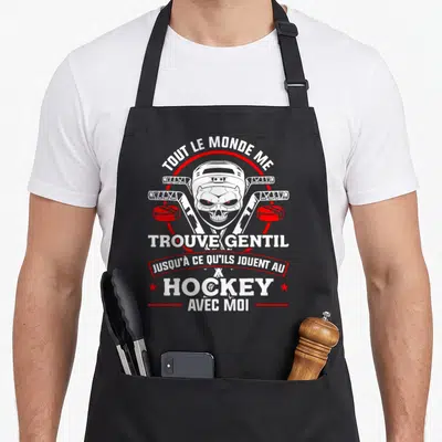 Tablier de cuisine noir avec un crâne en casque de hockey et deux crosse croisées sur fond gris uni.