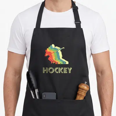 Tablier de cuisine noir avec joueur de hockey sur terrain en silhouettes colorées et texte HOCKEY