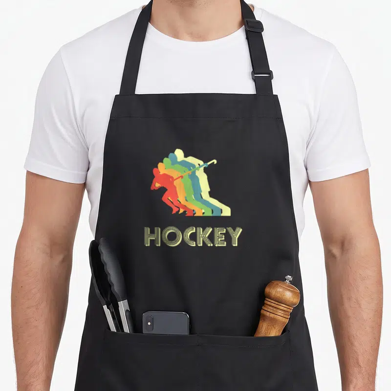 Tablier de cuisine noir avec joueur de hockey sur terrain en silhouettes colorées et texte HOCKEY