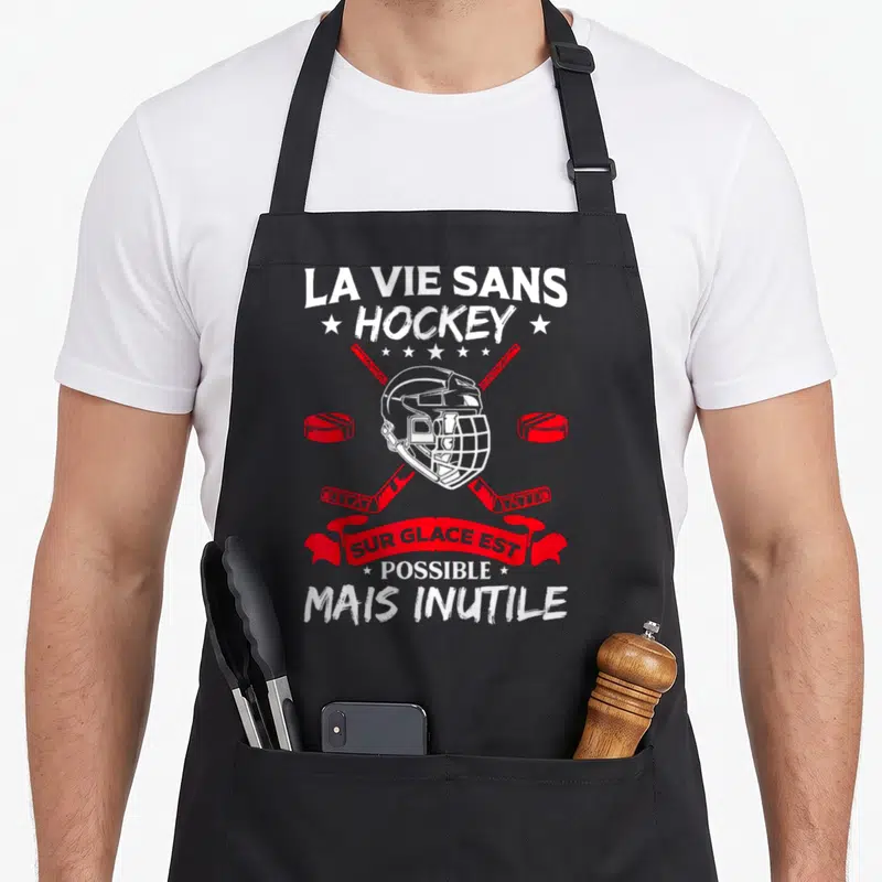 Tablier de cuisine noir avec casque de hockey, bâtons croisés et dicton humoristique en blanc et rouge.