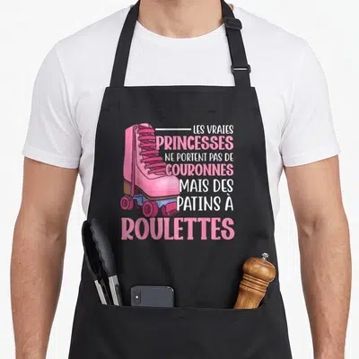 Tablier de cuisine noir avec une illustration de patin rose et le texte Les Vraies Princesses ne portent pas de couronnes mais des patins à roulettes