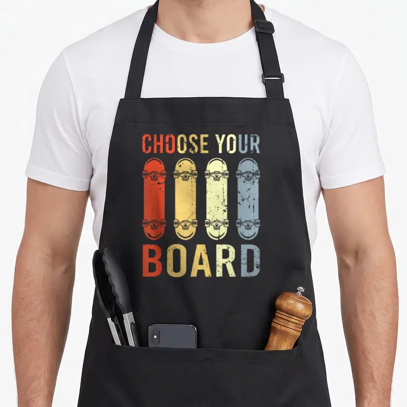 Tablier de cuisine noir avec quatre planches de skateboard vintage rouge, jaune, beige et bleu sous le texte Choose your board.