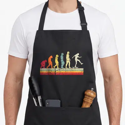 Tablier de cuisine noir avec illustration évolutive montrant un skateur final sur bandes colorées vintage.