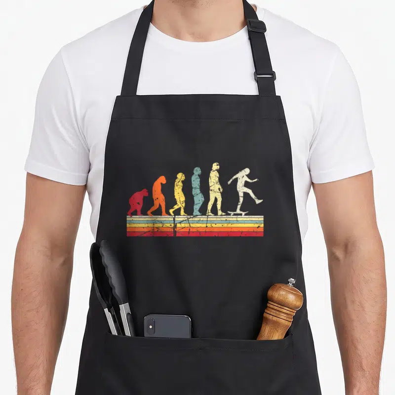 Tablier de cuisine noir avec illustration évolutive montrant un skateur final sur bandes colorées vintage.