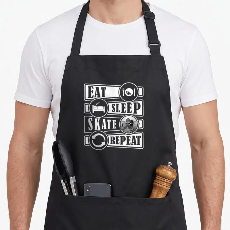 Tablier de cuisine noir avec inscription Eat Sleep Skate Repeat et icônes associées en blanc.