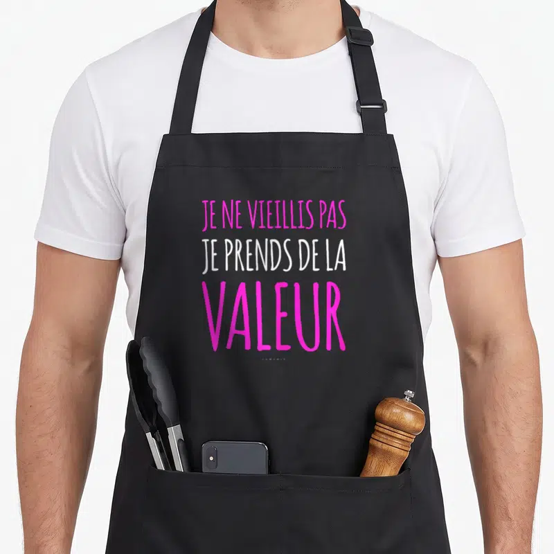 Tablier de cuisine noir avec l'inscription Je ne vieillis pas je prends de la valeur en rose et blanc.