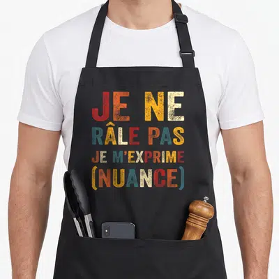 Tablier de cuisine noir avec le texte coloré Je Ne Râle Pas Je M'exprime Nuance imprimé au centre.