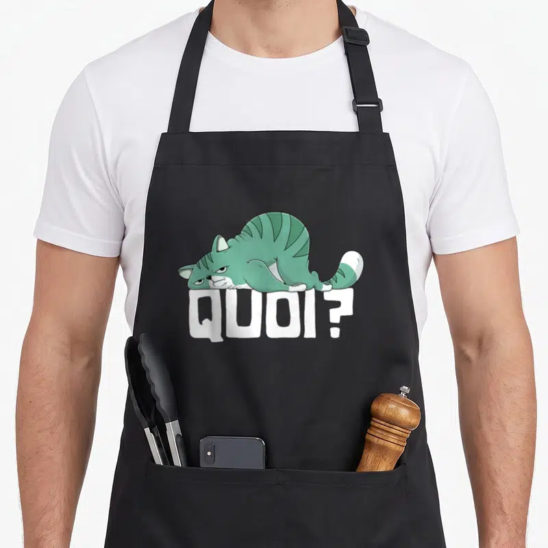 Tablier de cuisine noir avec illustration d'un chat vert posé sur le mot QUOI en lettres blanches épaisses.