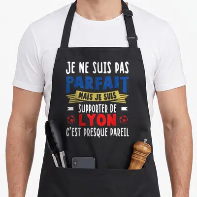 Tablier de cuisine noir avec linscription Je ne suis pas parfait mais je suis supporter de Lyon cest presque pareil en bleu rouge et jaune.