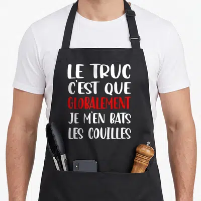 Tablier de cuisine noir avec l'inscription Le Truc C'est Que Globalement Je M'en Bats Les Couilles en typographie blanche et rouge.