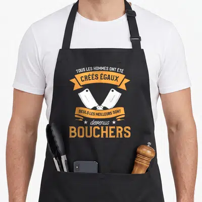 Tablier de cuisine noir avec deux haches de boucher croisées et une citation humoristique en orange et blanc sur fond uni.