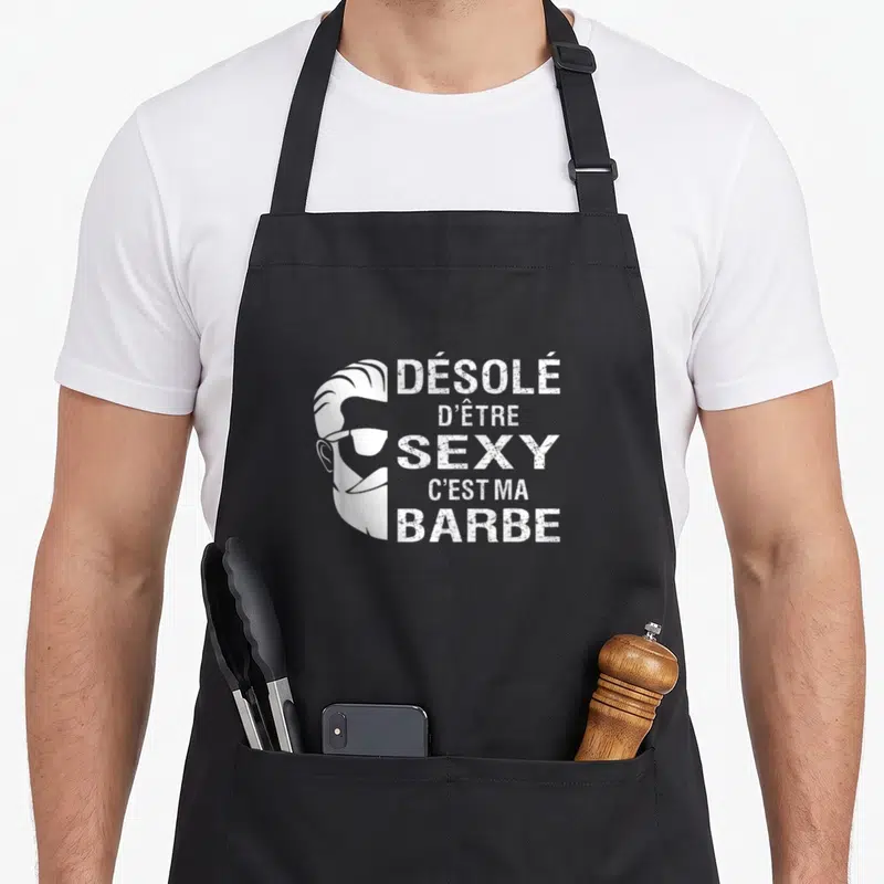 Tablier de cuisine noir avec une illustration blanche d'un visage barbu aux lunettes de soleil et un texte humoristique.