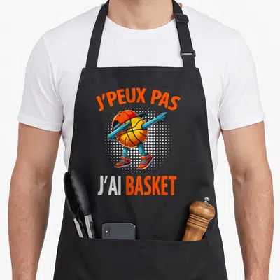 Tablier de cuisine noir avec un ballon de basket effectuant un dab et l'inscription J'peux pas j'ai basket en orange et blanc.