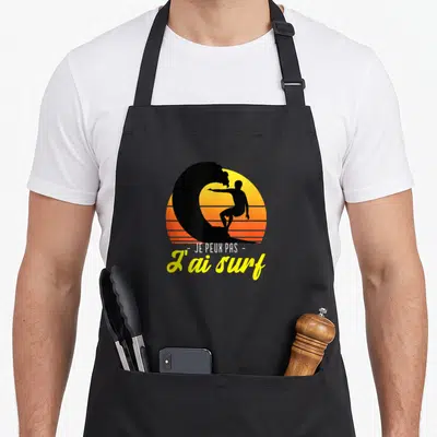 Tablier de cuisine noir avec silhouette surfeur et texte je peux pas j'ai surf sur fond de soleil orange.