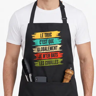 Tablier de cuisine noir avec le texte « Le truc c'est que globalement je m'en bats les couilles » sur fond de traits colorés.