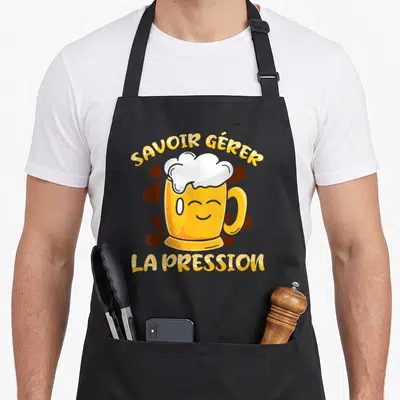 Tablier de cuisine noir avec illustration d'une bière souriante et texte Savoir Gérer La Pression en jaune.