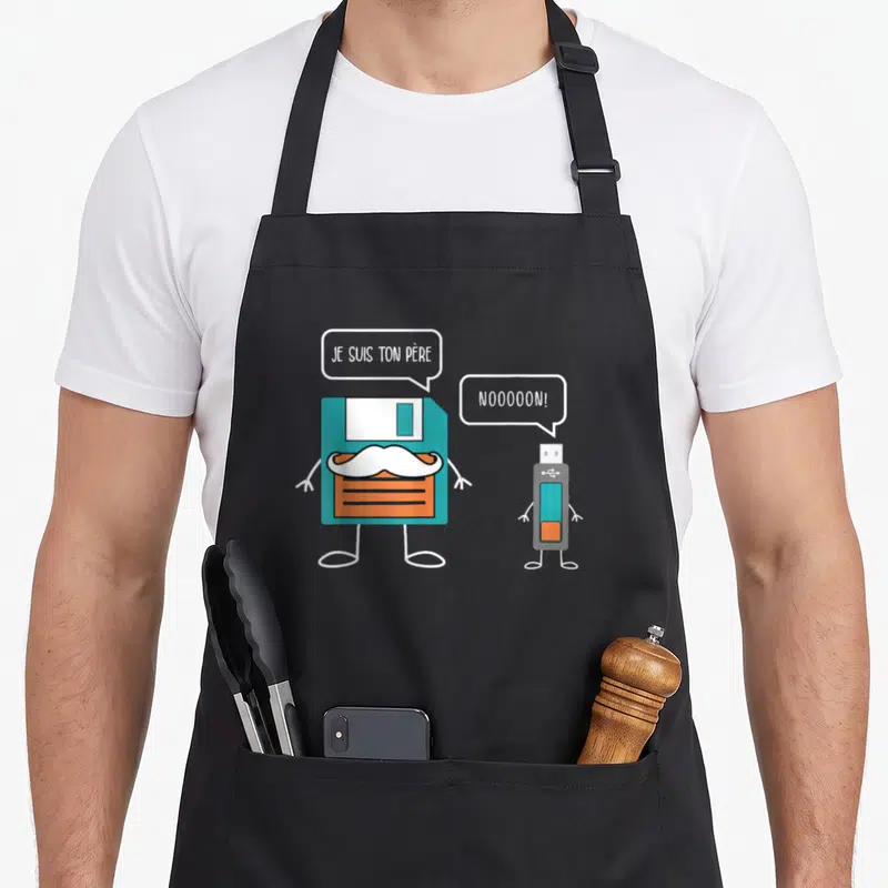 Tablier de cuisine noir avec illustration d'une disquette et une clé USB se disputant sur leur relation parentale.
