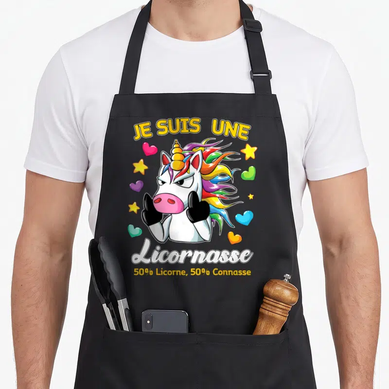 Tablier de cuisine noir avec une licorne aux doigts d'honneur entourée d'étoiles et de cœurs colorés.