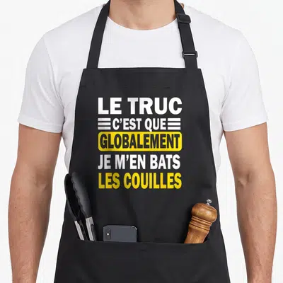 Tablier de cuisine noir avec le texte Le truc c'est que globalement je m'en bats les couilles en blanc et jaune.