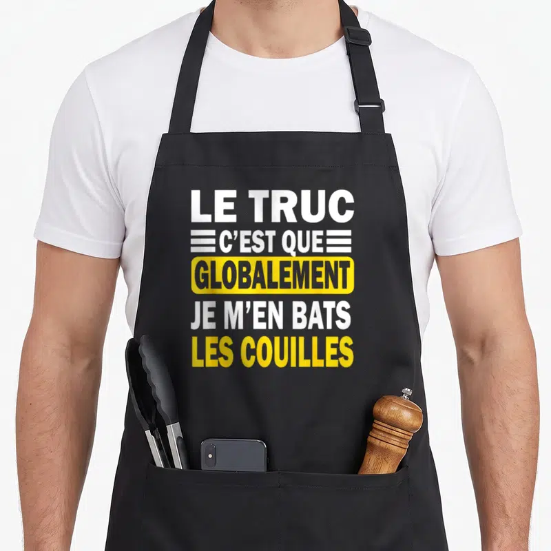 Tablier de cuisine noir avec le texte Le truc c'est que globalement je m'en bats les couilles en blanc et jaune.