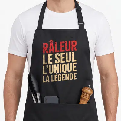 Tablier de cuisine noir avec l'inscription râleur le seul l'unique la légende en typographie rouge et beige.