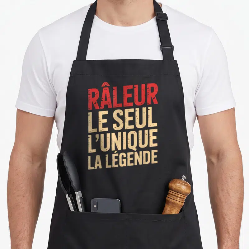 Tablier de cuisine noir avec l'inscription râleur le seul l'unique la légende en typographie rouge et beige.