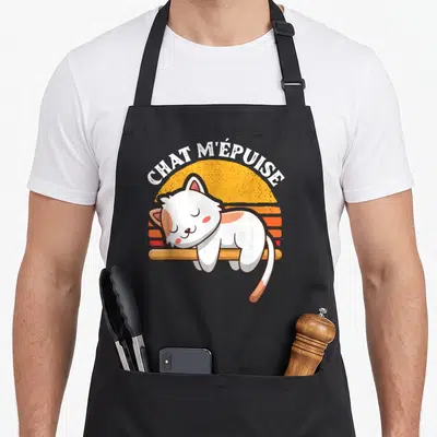 Tablier de cuisine noir avec illustration d'un chat blanc dormant sur une barre et le texte chat m'épuise en arc de cercle.