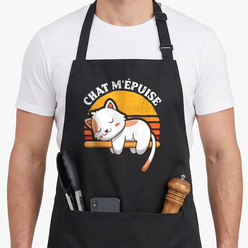 Tablier de cuisine noir avec illustration d'un chat blanc dormant sur une barre et le texte chat m'épuise en arc de cercle.