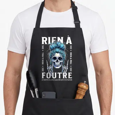 Tablier de cuisine noir avec illustration d'un crâne aux cheveux bleus en chignon et le texte rien à foutre en lettres blanches.
