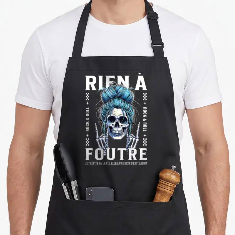 Tablier de cuisine noir avec illustration d'un crâne aux cheveux bleus en chignon et le texte rien à foutre en lettres blanches.