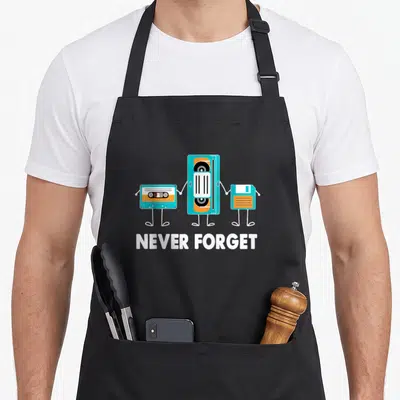Tablier de cuisine noir avec une cassette, une bande magnétique et un floppy disk tenant la main sous le texte Never Forget en blanc.