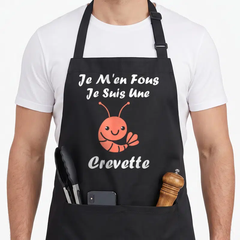 Tablier de cuisine noir avec une crevette rose souriante et le texte blanc Je M'en Fous Je Suis Une Crevette imprimé au centre.