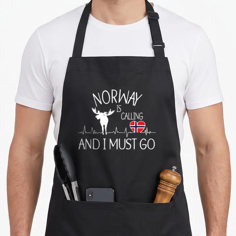 Tablier de cuisine noir avec silhouette de renne, cœur au drapeau norvégien et texte blanc en anglais.
