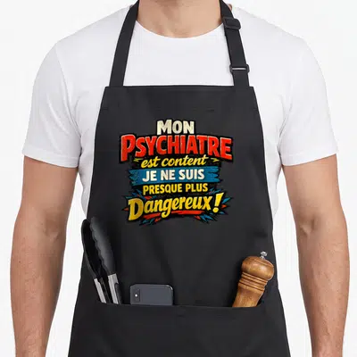 Tablier de cuisine noir avec l'inscription Mon psychiatre est content je ne suis presque plus dangereux en lettres colorées.