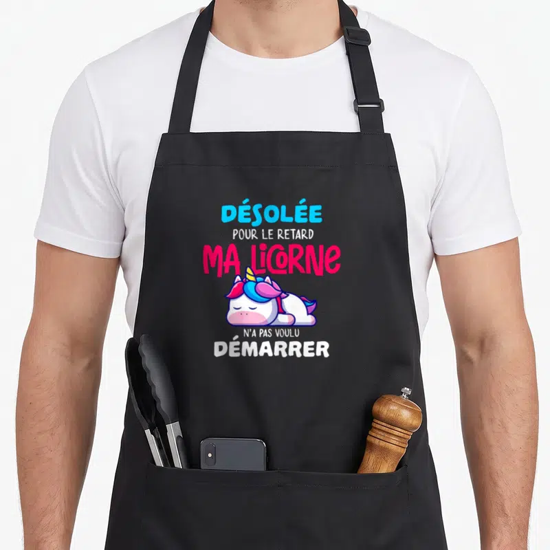 Tablier de cuisine noir avec une licorne rose et bleue endormie et un texte humoristique en lettres colorées.