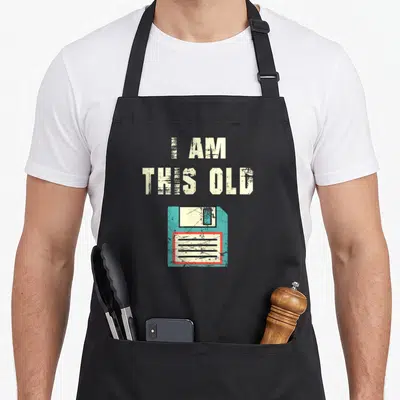 Tablier de cuisine noir avec inscription I am this old et illustration de disquette bleue usée.