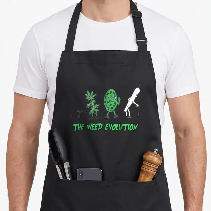 Tablier de cuisine noir avec illustration verte montrant l'évolution d'une plante en joint vieilli et le texte The Weed Evolution.
