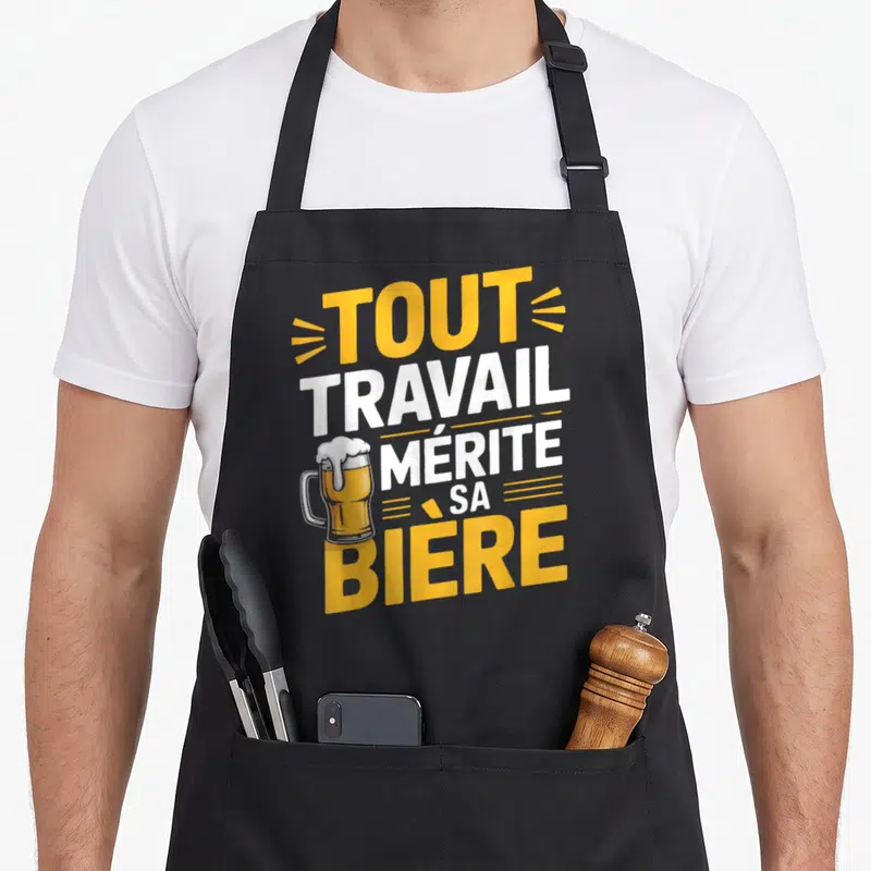 Tablier de cuisine noir avec l'inscription tout travail mérite sa bière et un dessin de mug de bière jaune et blanc.