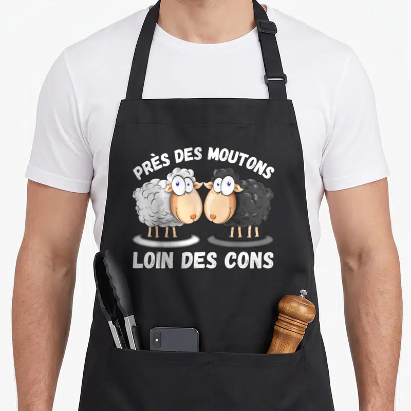 Tablier de cuisine noir avec deux moutons cartoon blanc et noir et une phrase drôle imprimée en blanc.