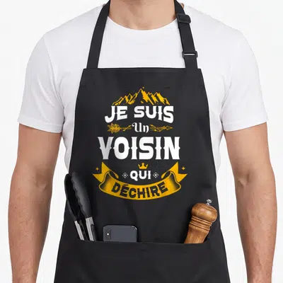 Tablier de cuisine noir avec inscription Je Suis Un Voisin Qui Déchire en blanc et or sur fond gris uni.
