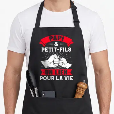 Tablier de cuisine noir avec deux poings se serrant et le texte Papi et Petit-Fils un lien pour la vie en blanc et rouge.
