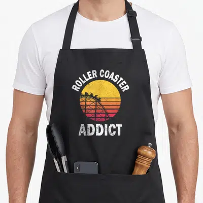 Tablier de cuisine noir avec illustration soleil vintage et texte roller coaster addict en blanc.