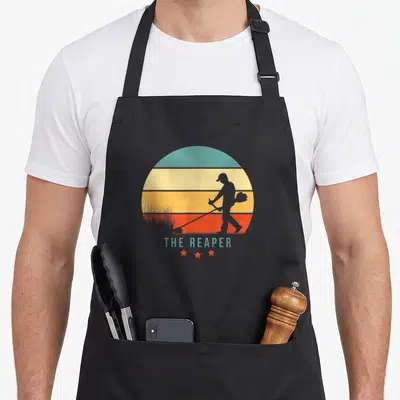 Tablier de cuisine noir avec silhouette homme débroussailleur sur fond sunset rétro et étoiles rouges.