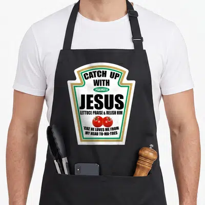Tablier de cuisine noir avec motif imitant une bouteille de ketchup blanc vert or et deux tomates rouges.