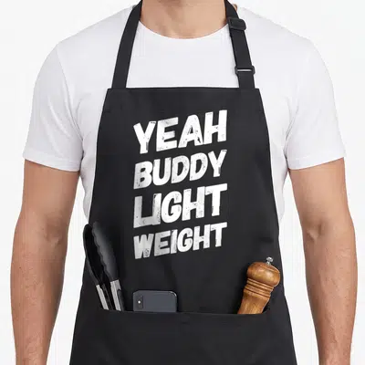 Tablier de cuisine noir avec l'inscription Yeah Buddy Light Weight en typographie blanche texturée.
