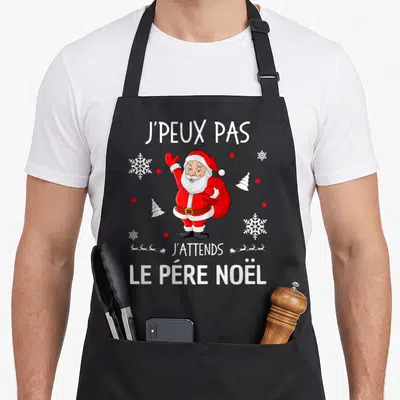 Tablier de cuisine noir avec illustration colorée du Père Noël levant la main et texte blanc j'peux pas j'attends le père noël.