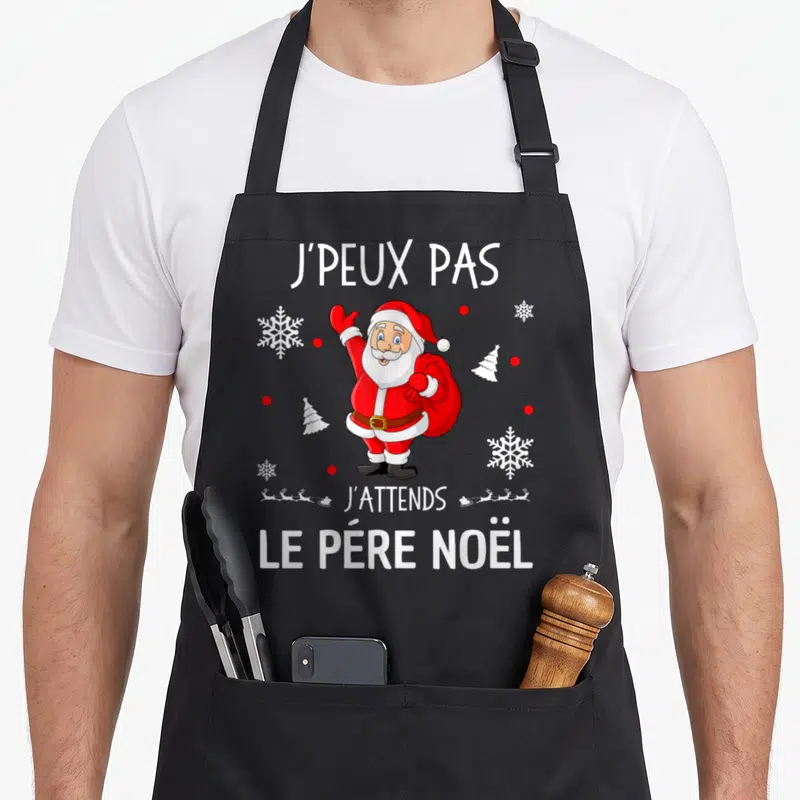 Tablier de cuisine noir avec illustration colorée du Père Noël levant la main et texte blanc j'peux pas j'attends le père noël.