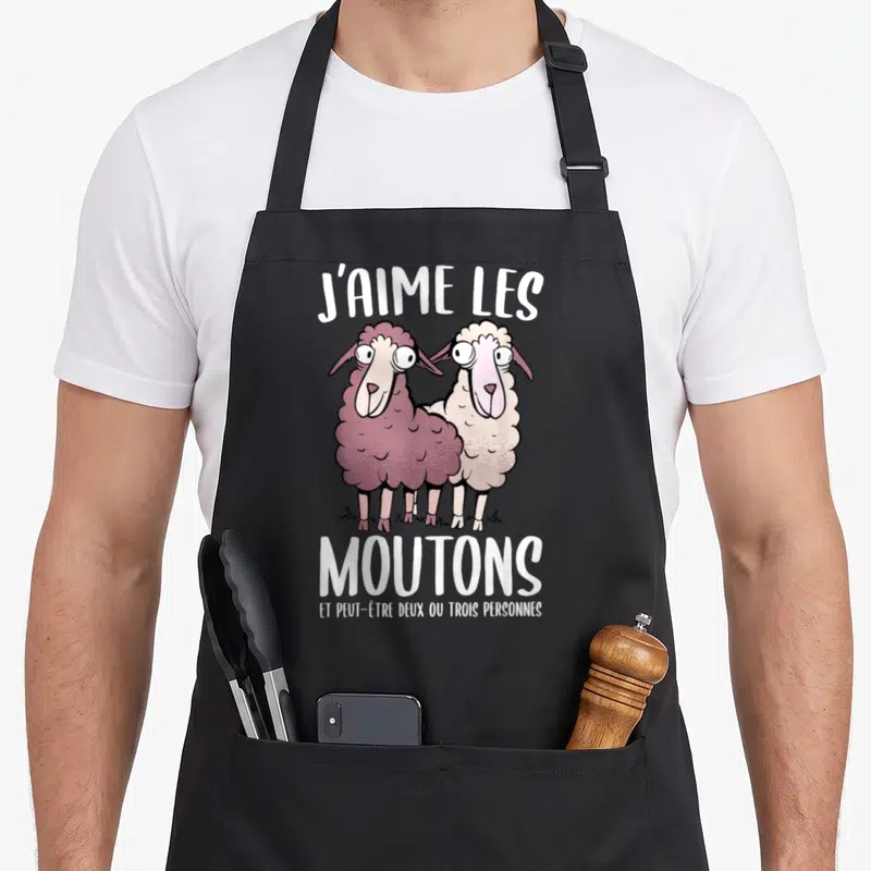 Tablier de cuisine noir avec deux moutons cartoon aux grands yeux et le texte J'aime les moutons imprimé en blanc au centre.