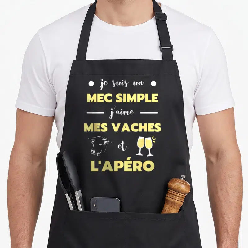 Tablier de cuisine noir avec texte jaune je suis un mec simple j'aime mes vaches et l'apéro illustré d'une tête de vache et deux verres.