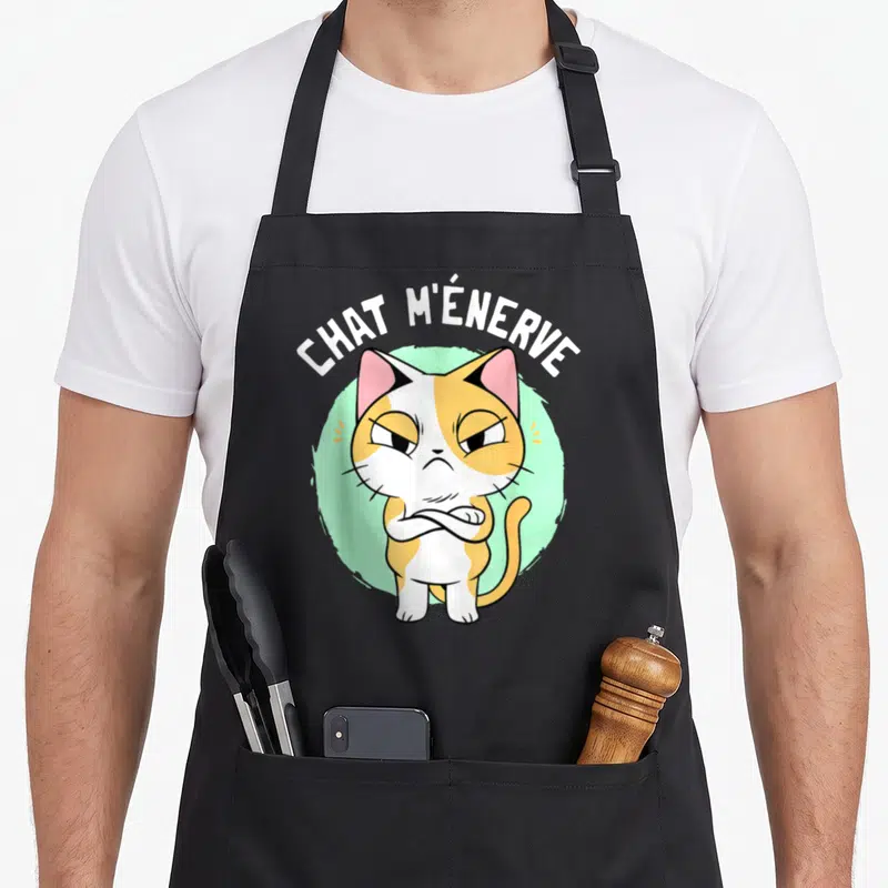 Tablier de cuisine noir avec illustration d'un chat tricolore aux bras croisés et le texte chat m'énerve en arc de cercle.